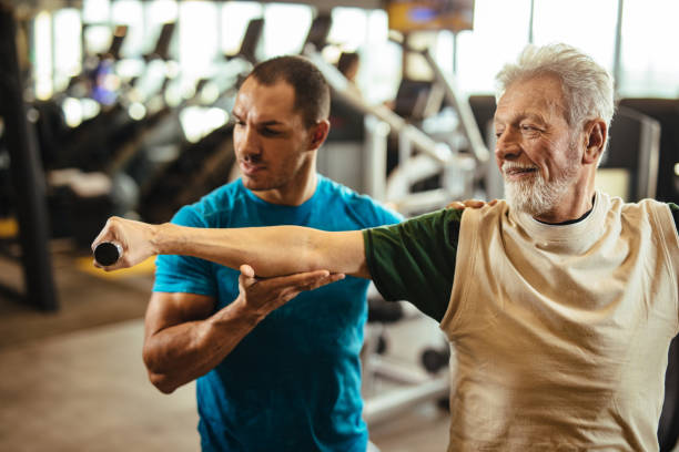 istock Senior man exercising with personal trainer using dumbbells at the gym 1223389023