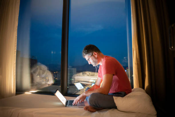 istock Man sits on a bed and uses a laptop at night 1223389394