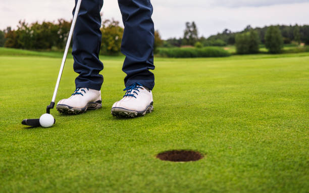 golf ball hitting on green and falling into hole stock photo