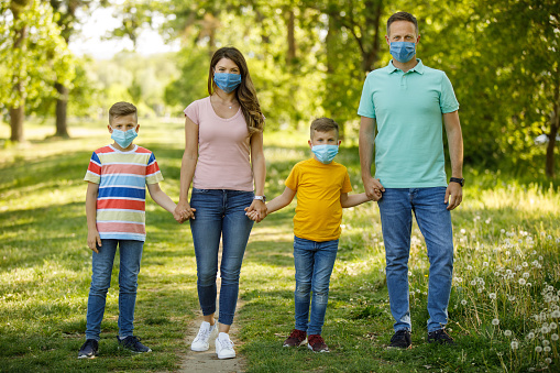Family walking in the city park wearing anti virus masks and holding hands