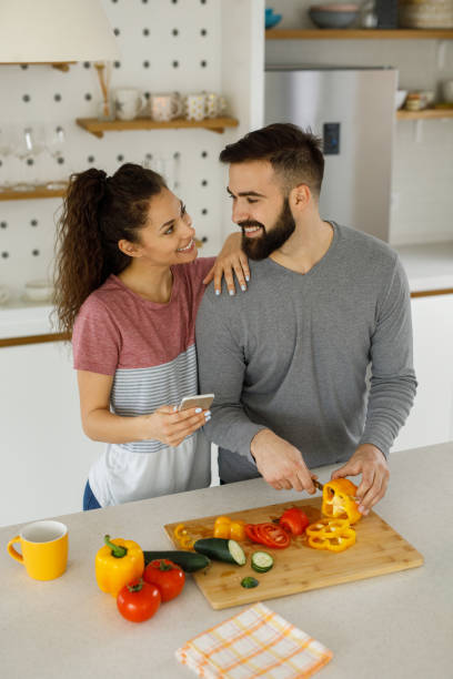 istock Young woman using her smart phone while her boyfriend prepares a meal 1223392583