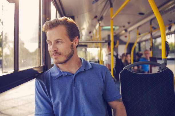 Mid adult man traveling in bus. Male passenger is commuting by public transport, looking through window.