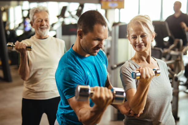 istock Senior couple exercising with personal trainer using dumbbells at the gym 1223392813
