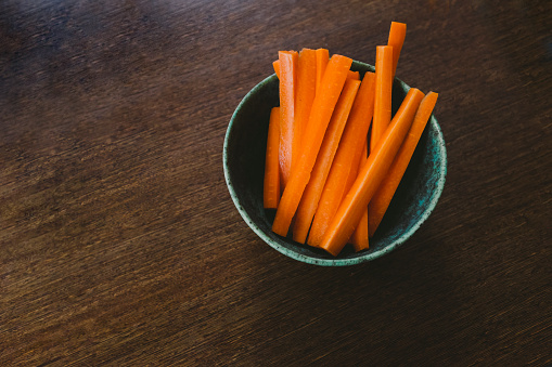 May 6, 2020 - Warsaw, Poland: healthy children snack - fresh carrots sticks, fingers in a bowl on a dark wooden table, low key, healthy eating.