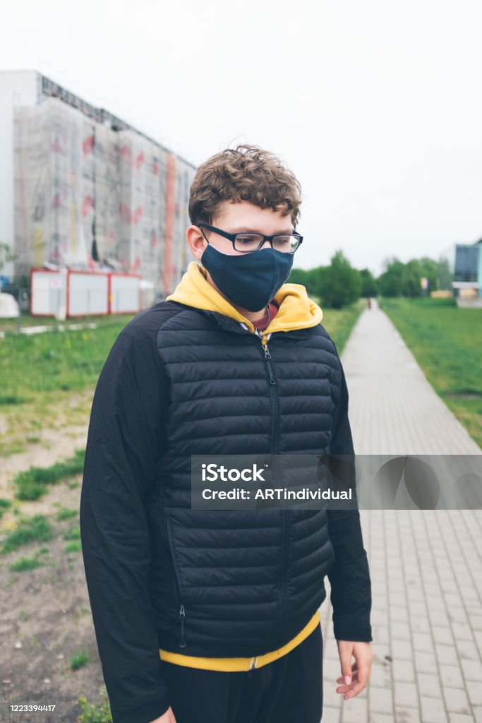 cute sad teen boy in linen cloth homemade face mask during corona virus pandemic in Warsaw, Poland May 6, 2020 - Warsaw, Poland: Sad teenage boy wearing protective face mask in the time of covid-19 pandemic looking sad, tired, worried, unhappy while standing outdoors Adolescence Stock Photo
