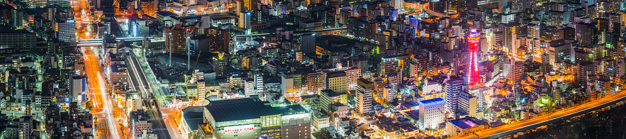 Aerial panorama photograph over the iconic Tsutenkaku Tower and glittering neon night cityscape of Shinsekai in the heart of downtown Osaka, Japan.