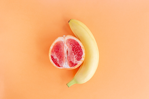 Yellow banana and grapefruit on a pastel orange background, marital love concept