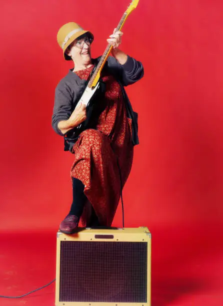 Photo of Senior woman, foot on amp, rocks her electric guitar