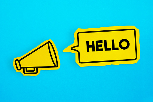 Megaphone drawing on the cut yellow paper makes “Hello” announcement. Horizontal composition with copy space. Communication Concept.