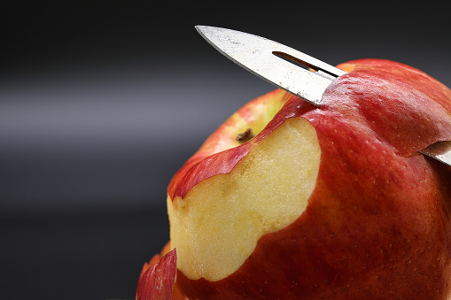 peeling apple in kitchen. peel apple with pocket knife. dark background. close up