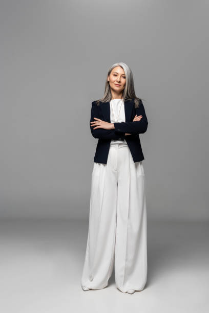 mujer de negocios asiática confiada con el pelo gris y los brazos cruzados en gris - bien vestido fotografías e imágenes de stock