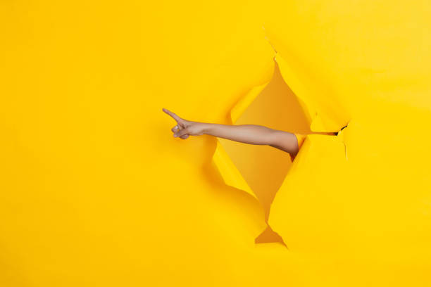 istock Female hand pointing in torn yellow paper hole background, celebration 1223411485