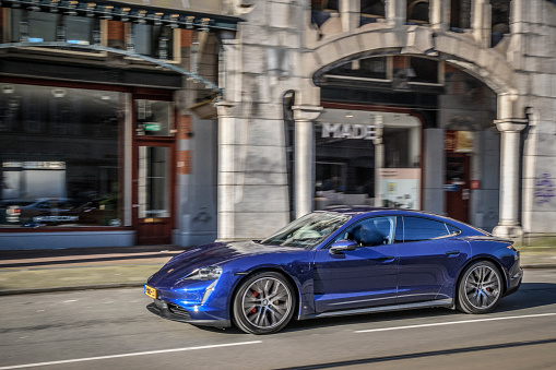 Porsche Taycan Turbo S all-electric luxury performance car driving on the street in Amsterdam during a sunny springtime morning. The Taycan is fitted with a battery-electric drivetrain of permanent-magnet synchronous motors on the axles, making the car all-wheel drive.