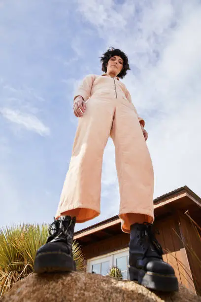 Portrait of a stylish young woman in a jumpsuit and platform boots standing on a rock outside against a blue sky