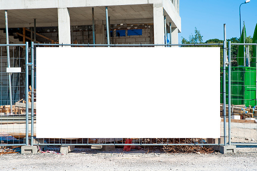 Blank white banner for advertisement mounted on the fence of construction site on a sunny day.