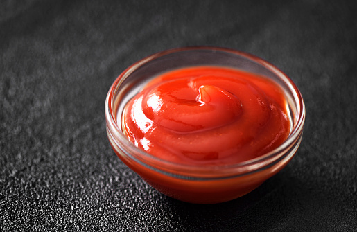Ketchup in a small glass bowl on a black background