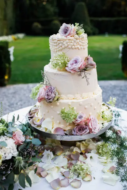 Wedding cake outside. Lots of flowers. On the background of greenery.