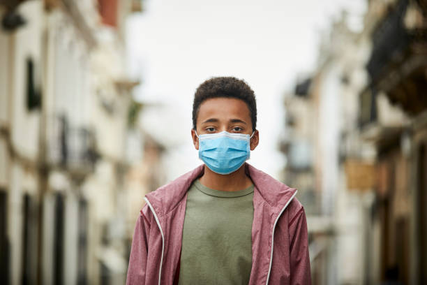 adolescente afroamericano con maschera protettiva per strada per pandemia di covid-19 - afro americano immagine foto e immagini stock