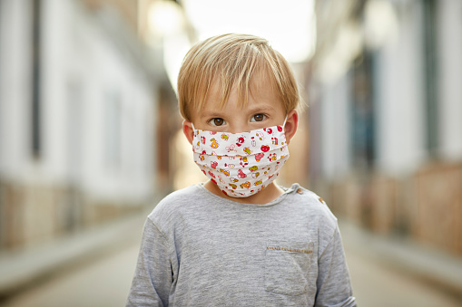 Young boy with hand made face mask standing on the street. Boy wearing face mask for coronavirus pandemic.