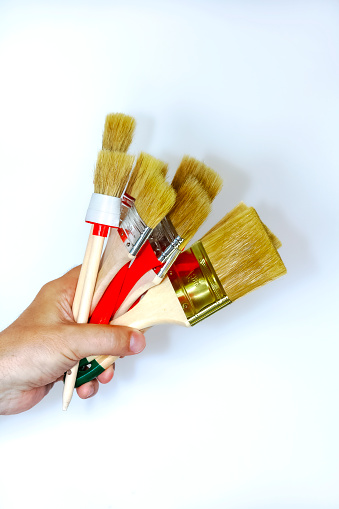 Artist hand with brush for painting. Hand holding a thick brushes isolated on a light background. A new miscellaneous paint brushes with hand in closeup