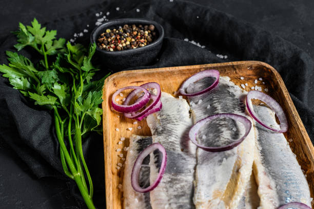 istock Marinated herring fillet with pepper, herbs and red onion. Black background. Top view 1223430041