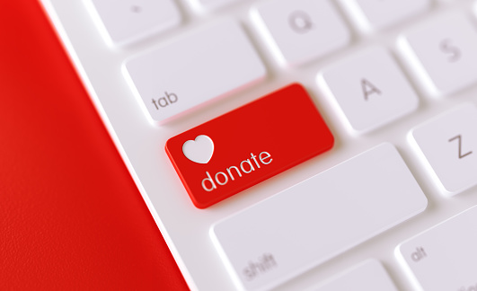 Donate icon written on a red button of a computer keyboard. Horizontal composition with selective focus and copy space. High angle view. Horizontal composition with copy space. Donation concept.
