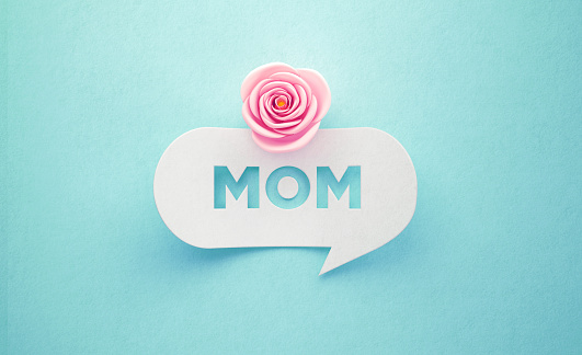 Pink rose sitting over a mom written speech bubble on turquoise background. Horizontal composition with copy space. Mother's Day concept.