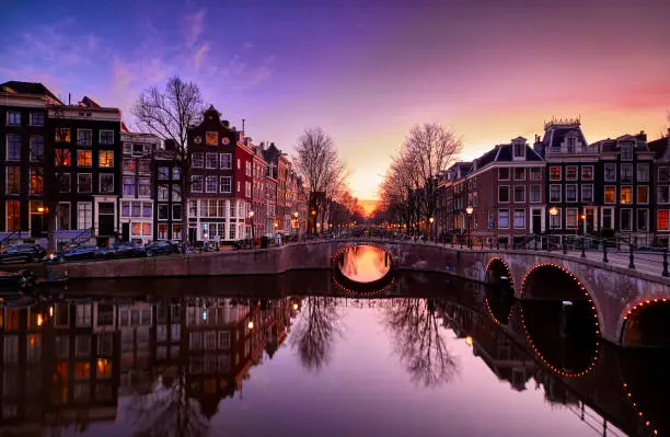 Amsterdam canals and typical canal houses in the old part of the city at dusk, the city lights are on. The streets are empty because of the lockdown, corona virus.