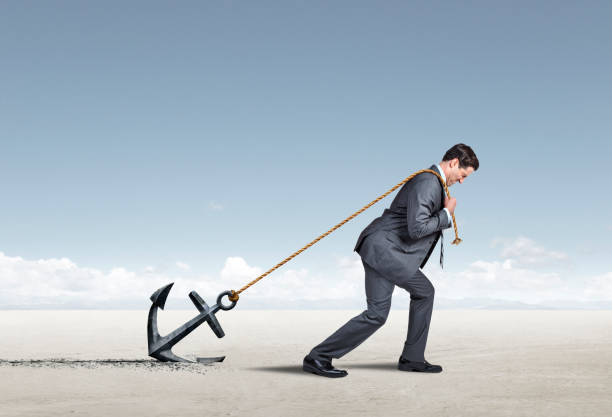 Burdened Man Drags An Anchor A businessman is burdened with the prospect of pulling on a rope that is tethered to an anchor as he attempts to drag it on his way to his destination. dragging photos stock pictures, royalty-free photos & images