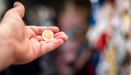 POSITANO, ITALY - April 21 2018: A hand holding a 2 euro coin on a colourful blurred background