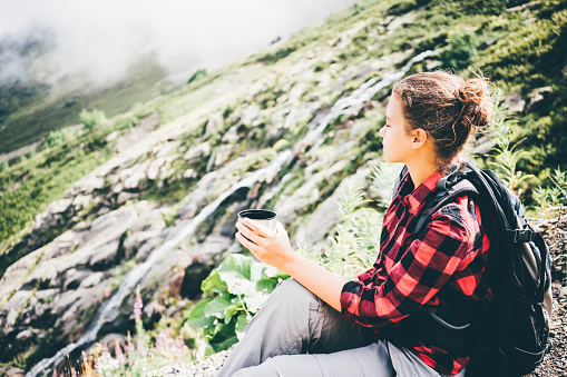Traveler girl drinking tea from thermos cup, outdoors.Traveler young woman resting in the mountains and drinking tea from thermos.
