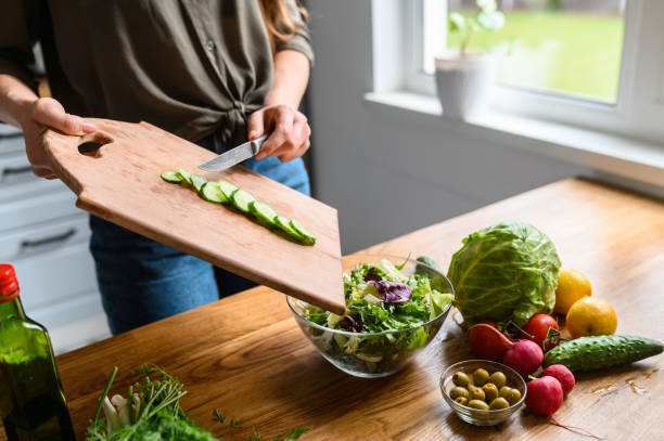 Girl throws sliced fresh cucumber in salad