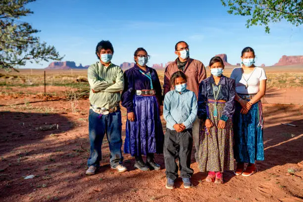 A Navajo family with the Monument Valley behind them stand together wearing masks for protection during the Coronavirus pandemic