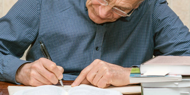 istock old elderly man writing with pen in rihgt hand books pile on table knowledge concept 1223444640