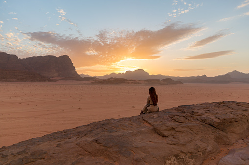 The girl sits on a rock and admires the wonderful sunset. Back view. Shot in Jordan. Wadi Rum Desert.