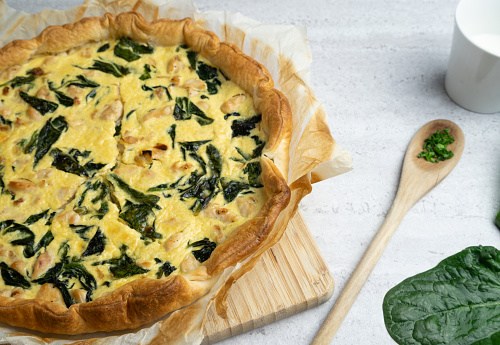 Quiche filled with chicken, chard with wooden spoon on soft background