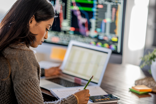 Middle Eastern woman tracking and trading stocks using laptop and desktop computer. Stock Exchange, investment, and financial trading concept.