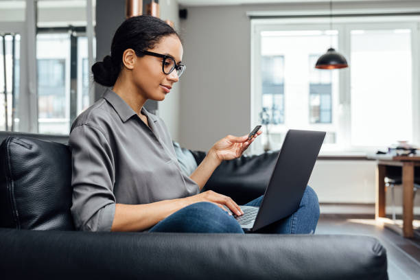 ung kvinna gör online betalning medan du sitter i vardagsrummet på soffan - online shopping bildbanksfoton och bilder