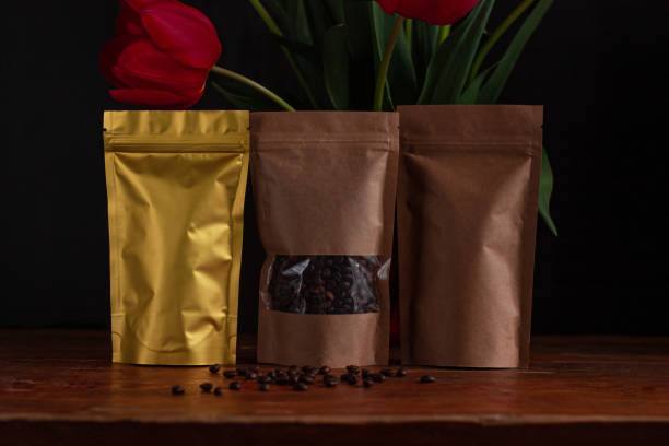 Pouch bags for coffee and tea with amazing blooming red tulips bouquet on black background. Food shop packaging mockup. Pouch bags for coffee and tea with amazing blooming red tulips bouquet on black background. Food shop packaging mockup. Foiled metal and kraft paper packs. Dark moody low key flowers banner copy space Slective Focus stock pictures, royalty-free photos & images