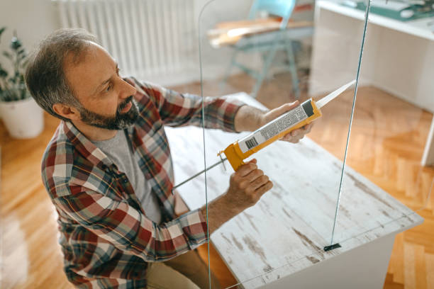 Man caulking a glass partition Man applying silicone sealant with caulking gun while installing a transparent glass partition at home sealant photos stock pictures, royalty-free photos & images