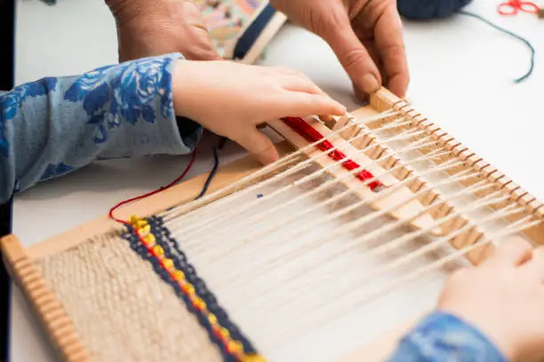 A little girl learns process to weave thick threads. Hands close up. Creating a picture by weaving.