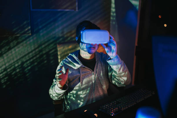 istock an asian chinese male put on VR goggle and experiencing 3D virtual gaming experience in his home office study room at night in front of his desktop PC 1223479564