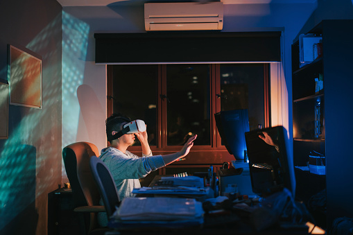 an asian chinese male put on VR goggle and experiencing 3D virtual gaming experience in his home office study room at night in front of his desktop PC
