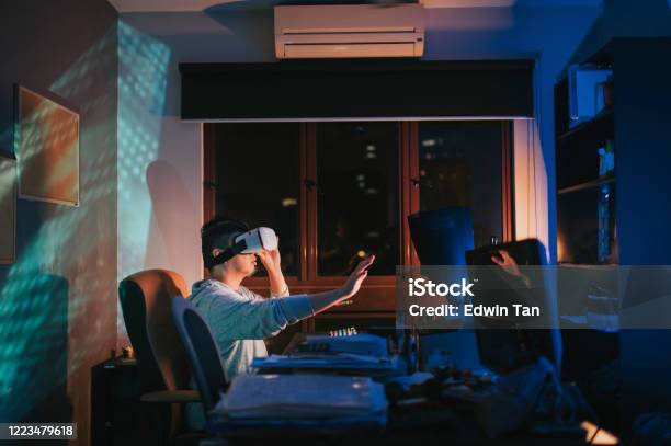 An Asian Chinese Male Put On Vr Goggle And Experiencing 3d Virtual Gaming Experience In His Home Office Study Room At Night In Front Of His Desktop Pc Stock Photo - Download Image Now
