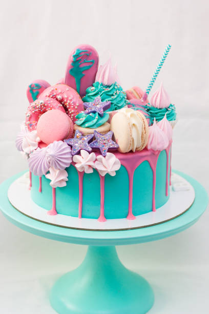 розовый и бирюзовый торт, украшенный макаронами, кексами, тортовыми поп-музыками, безе, эскимо и расплавленным шоколадом. - кусок торта фотографии стоковые фото и изображения