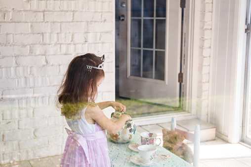 The young girl, dressed as a princess, pretends to have tea with her toy bear.