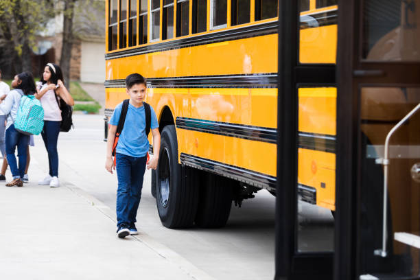 istock While girls talk in background, boy walks beside school bus 1223481684