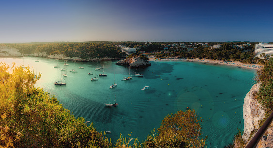 Panoramic view of the beautiful Cala Galdana on the southern coast of Menorca, part of the Balearic Archipelago in the Mediterranean Sea. Numerous sailing boat are moored in the bay.