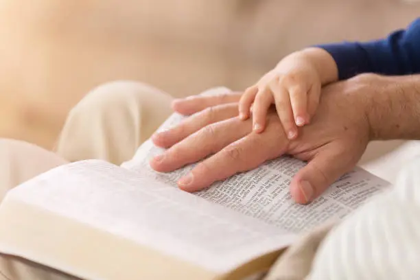 Photo of Grandpa Reading to Baby Boy From the Bible