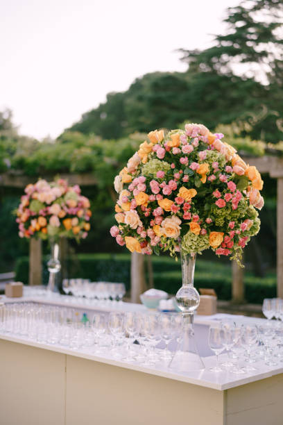 istock Wedding dinner table reception. Huge bouquets of yellow, pink, orange roses and green hydrangeas in a glass vase on a high leg. Large bouquets in the shape of a ball. A bar with lots of glasses. 1223487437